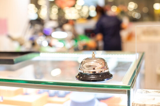 Selective focus to classic chrome service call bell placed on a glass counter desk with a warm blurred background, ready for customer assistance in a retail store, hotel reception, or office desk.