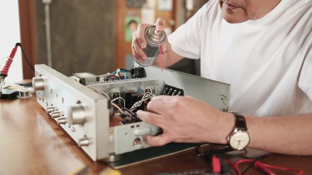 Close-up of man disassembling and checking audio equipment, spraying contact cleaner, cleaning circuit board for repair, home appliance DIY fix, electronics component hobby, handyman skill workshop.