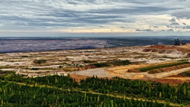 Aerial view of the vast Hambach open-pit mine with exposed earth layers, industrial machinery, and surrounding forest under a cloudy sky in Elsdorf, Nordrhein-Westfalen, Germany.