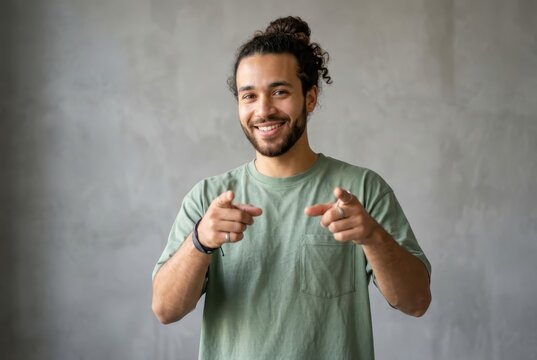 Confident Smiling Young Mixed-Race Man Pointing at Camera with Both Hands against Grey Wall