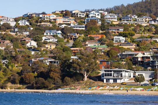 Houses densely scattered over a coastal hill with beach and water in the foreground at Blackmans Bay