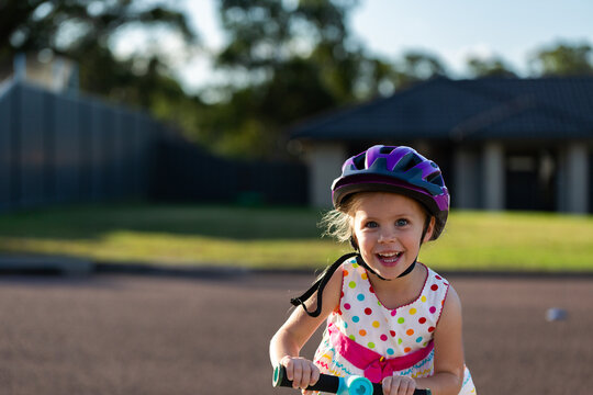 Happy Australian preschooler girl riding scooter in front yard of suburban home