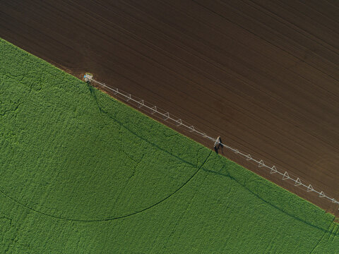 Irrigation sprinkler alongside lush green paddock with tilled land of fertile soil