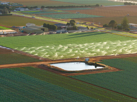 Distant aerial view of a dam and irrigation sprinklers amid a green market garden