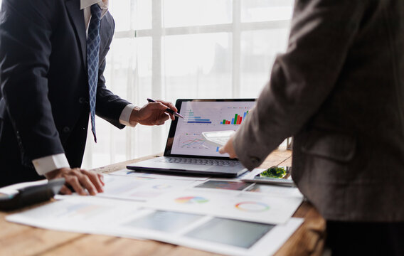 Business professionals analyzing financial data on laptop screen, collaborating on market strategy, discussing corporate reports, and planning successful investment goals