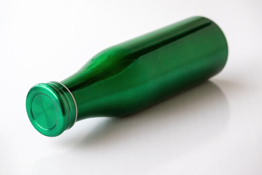 Metallic green water bottle lying down on clean white table surface. Reusable stainless steel container for daily personal hydration, travel, and fitness.