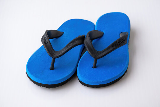 Pair of new blue rubber flip flops with black straps placed on white background. Casual daily footwear for home use, bathroom wear, and summer comfort.