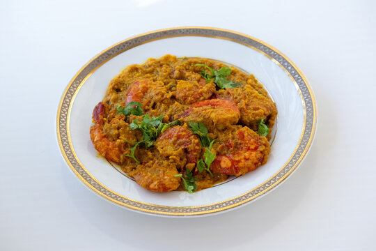 Freshly cooked Chingri malai curry in white plate on light background. Authentic coconut prawn curry dish from Asian cuisine culture.