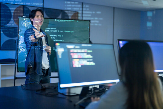 Asian male programmer giving coding presentations to IT team in the modern office. Tech startup developer explaining software on screens. Corporate innovation and digital technology business concepts