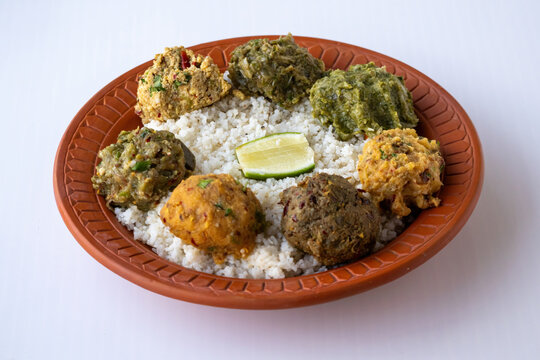 Authentic Bangladeshi steamed rice platter surrounded by traditional spicy mashed dishes including aloo, begun, chepa shutki, dim, and borboti bhorta with a lemon slice for lunch.