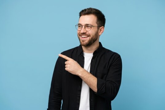Happy Young Bearded Man in Glasses Pointing Finger Aside at Copy Space on Blue Background