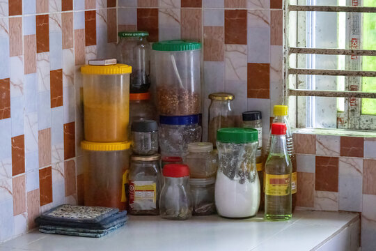 Various Glass Spice Jars, Plastic Containers, Oil Bottles and Cooking Seasonings Placed on Tiled Kitchen Countertop Corner, Home Kitchen Storage.