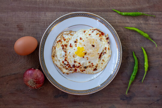 Delicious Fried Eggs Sunny Side Up with Chili Flakes, Ceramic Plate, Whole Raw Egg, Red Onion, Spicy Chili Ingredients, Traditional Bengali Breakfast. Top view.