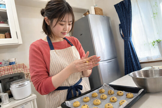 家庭の台所でストライプ柄エプロンを着けチョコチップ生地を丸める女性