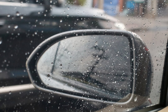 Raindrops on car window obscuring side mirror view during a drive