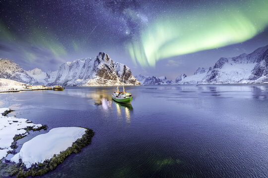 spectacular Green Aurora Borealis glowing over a snowy Arctic fjord and mountains at night with fishing trawler