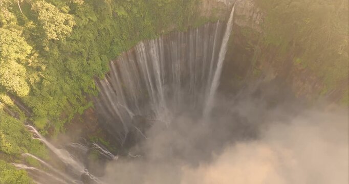 Aerial view of Tumpak Sewu Waterfall with cascading water falling over steep cliffs surrounded by lush tropical greenery in Kecamatan Pronojiwo, Jawa Timur, Indonesia.