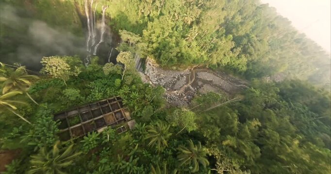 Aerial view of Tumpak Sewu Waterfall surrounded by lush tropical jungle and palm trees in Kecamatan Pronojiwo, Jawa Timur, Indonesia.
