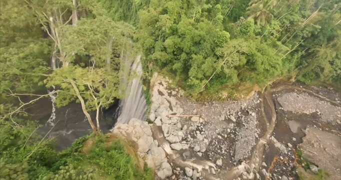 Aerial view of Tumpak Sewu Waterfall surrounded by lush tropical rainforest and rocky riverbed in Kecamatan Pronojiwo, Jawa Timur, Indonesia.