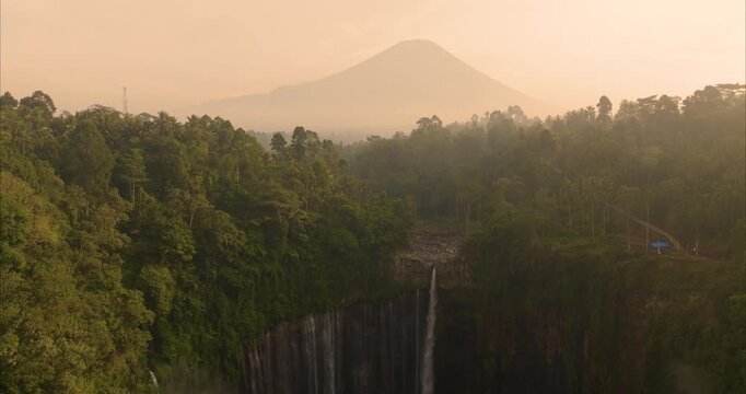 Aerial view of Tumpak Sewu Waterfall surrounded by lush tropical forest and misty mountains in Kecamatan Pronojiwo, Jawa Timur, Indonesia.