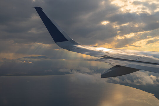 The wing of a passenger plane above picturesque clouds and sunbeams, over Kyrgyzstan's Lake Issyk-Kul.