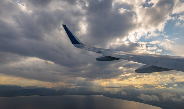 The wing of a passenger plane above picturesque clouds and sunbeams, over Kyrgyzstan's Lake Issyk-Kul.