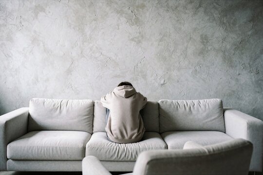 Person sitting alone on sofa with back turned to camera indoors