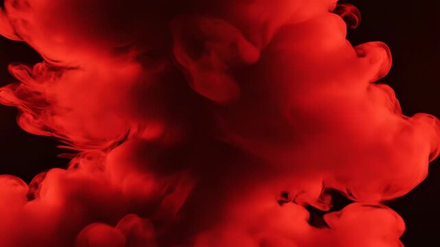 Vibrant red smoke swirling and billowing against a dark black background, dense plumes of colored vapor creating abstract fluid shapes and textured clouds in slow motion.