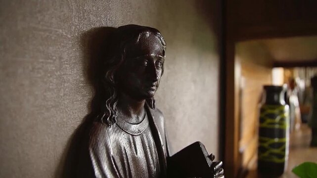 Religious wooden carving of Jesus Christ holding bible on wall in cinematic lighting.