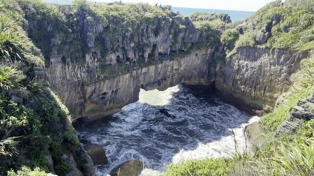 Ocean water surges through a narrow chasm in layered rock cliffs, shown in slow motion