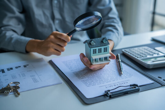 Asian businessman holding magnifying glass examine house model real estate invesment concept