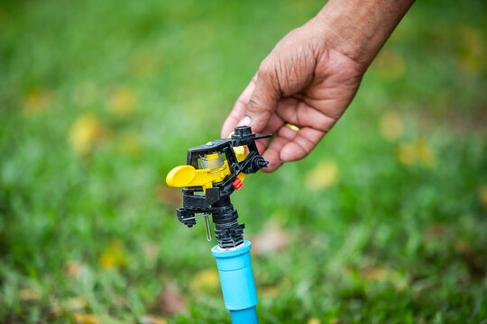 Selective focus to gardener adjusting a yellow and black water sprinkler nozzle in a green garden lawn. Ideal for irrigation, lawn care, agriculture, and water management.