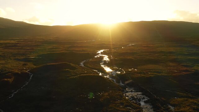 Aerial view of a winding stream flowing through the rugged moorland of Skye at sunset in Highland Council, Scotland, United Kingdom.