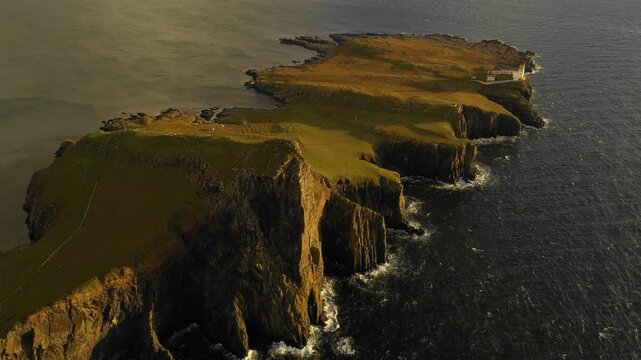Aerial view of Neist Point Lighthouse on the cliffs of the Isle of Skye, with dramatic coastal rock formations and the deep blue sea in Highland Council, Scotland, United Kingdom.
