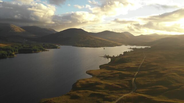 Aerial view of the Isle of Skye landscape featuring a serene lake surrounded by rolling hills and golden hour light in Highland Council, Scotland, United Kingdom.