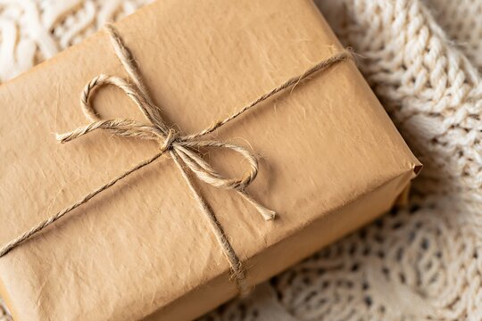 Small gift box wrapped in brown paper with twine string sitting on a soft knitted fabric