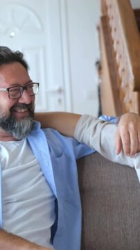 Cheerful father and his smiling teenage son having fun together, chatting and laughing while sitting on the sofa at home, enjoying a beautiful moment of family connection and love