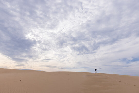 A small hiker stand on the ridge of a sand dune with a vast sky behind them