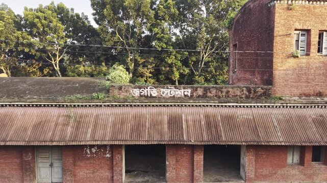Static drone shot of Jagati Station red brick facade with faded Bengali signboard in Bangladesh