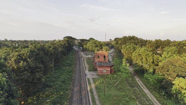 Late afternoon drone flyover of abandoned two‑storey rail building in overgrown forested countryside Bangladesh