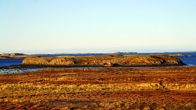 A low rocky islet sits in calm coastal waters surrounded by golden autumn tundra under a clear sky in Iceland