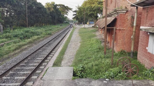Late day view along old red railway station platform with cobbled path, grass and distant people in rural Bangladesh