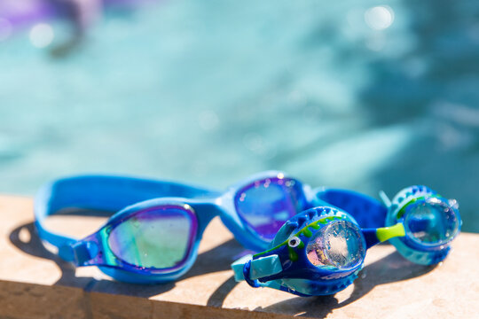 Two pairs of blue swimming goggles resting on the edge of a pool