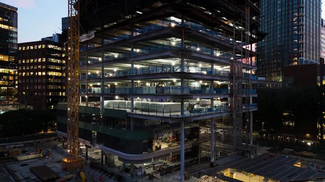 Aerial view of a modern building under construction at night with a tall crane and illuminated steel framework in Boston, Massachusetts, United States.