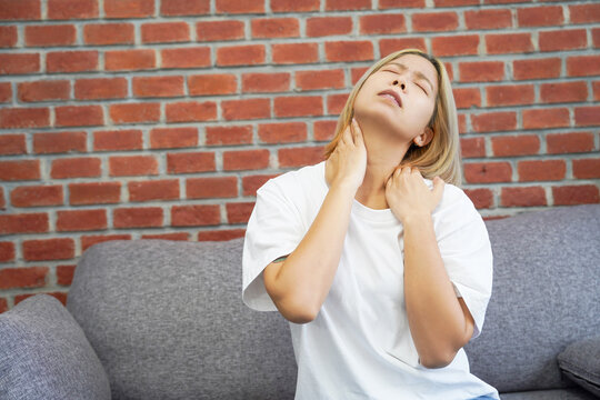 Asian young woman suffering neck pain sitting on sofa couch after finished work at home