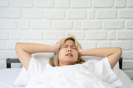 Upset and tired young woman lying on the bed in pajamas