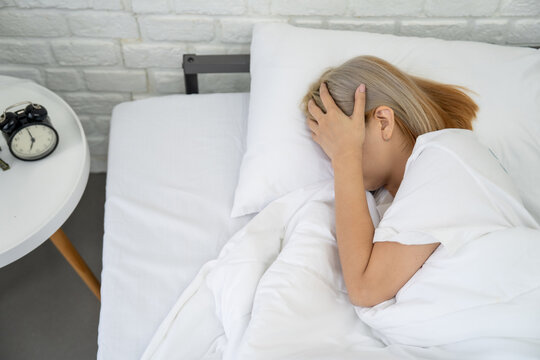 Asian woman lay on a bed, holding her head with her hand. She was experiencing a headache from life problems.