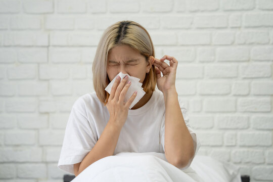 Young Asian woman felt a headache and discomfort while lying on the bed in her white bedroom.
