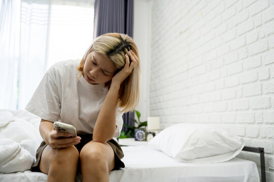 Asian woman is disappointed after a phone call at night, she sits on the bed in her bedroom.