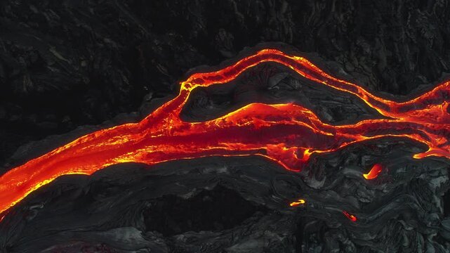 Aerial view of glowing lava flowing through dark volcanic rock at Kilauea volcano in Hawaii County, Hawaii, United States.